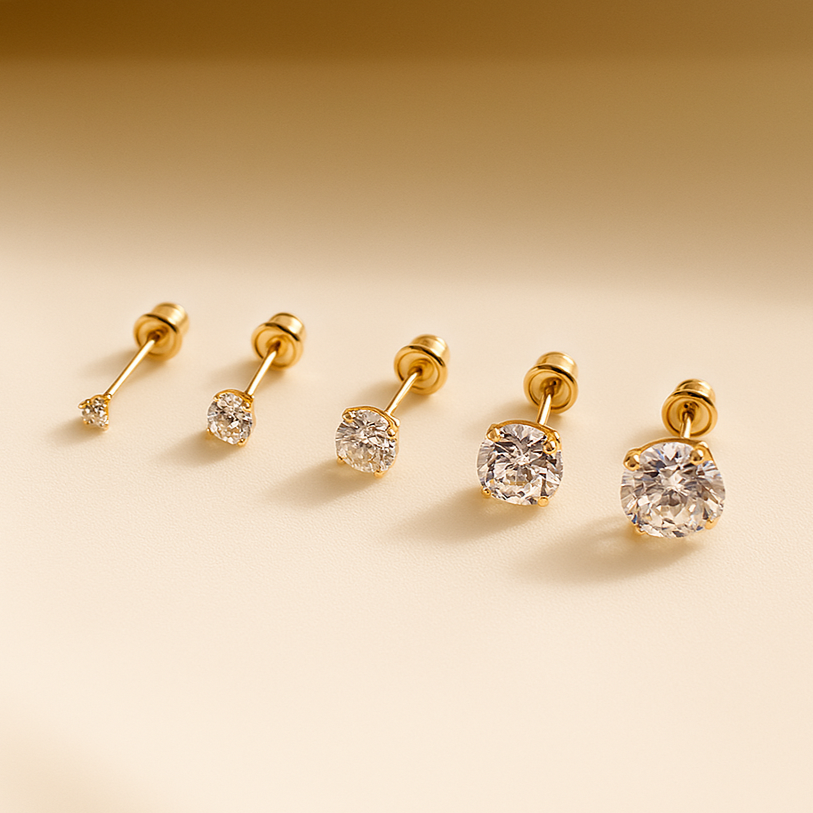 Set of gold earrings with clear gemstones on a beige background